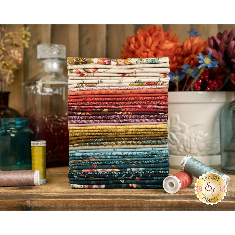 A stack of the fabrics included in the Dahlia FQ set, with flowers and a flower pot and bottles and thread.