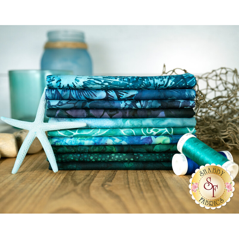 A stack of the fabrics available in the Oceanic Adventure FQ set, with jars and a net and thread and a starfish.