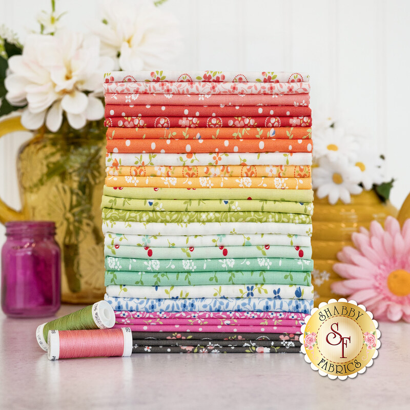 Stack of fabrics in the Cali & Co fat quarter set in shades of gray, green, white, orange, yellow, pink, and red, with pink and green thread and white florals in the background.