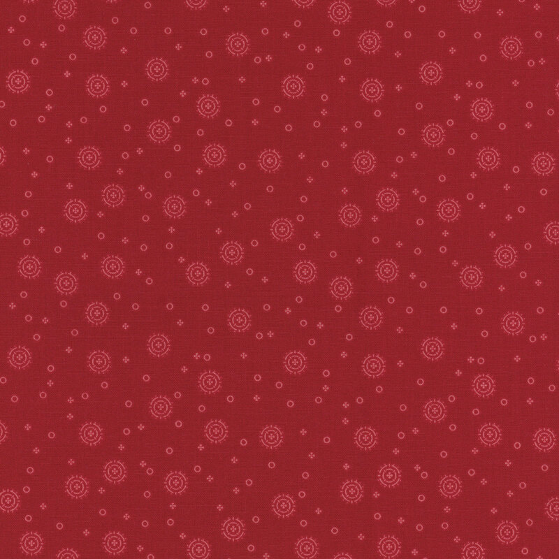 tonal red fabric with tiny circles and four-petaled flowers with larger circular sunbursts scattered across the fabric