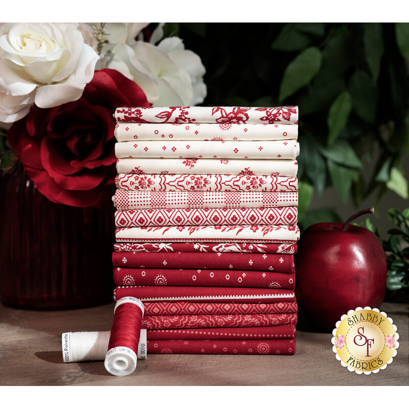 A stack of the fabrics in the Red Delicious 16 FQ set in shades of red and white, with flowers, thread, and an apple.