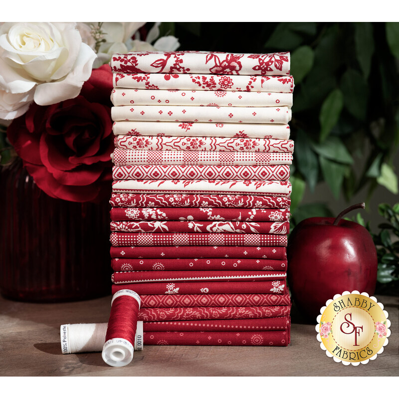 A stack of the fabrics in the Red Delicious 21 FQ set in shades of red and white, with flowers, thread, and an apple.