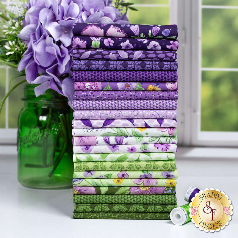 A photo of a stack of the fabrics in the Plum Petals fat quarter set in shades of purple, green, and white