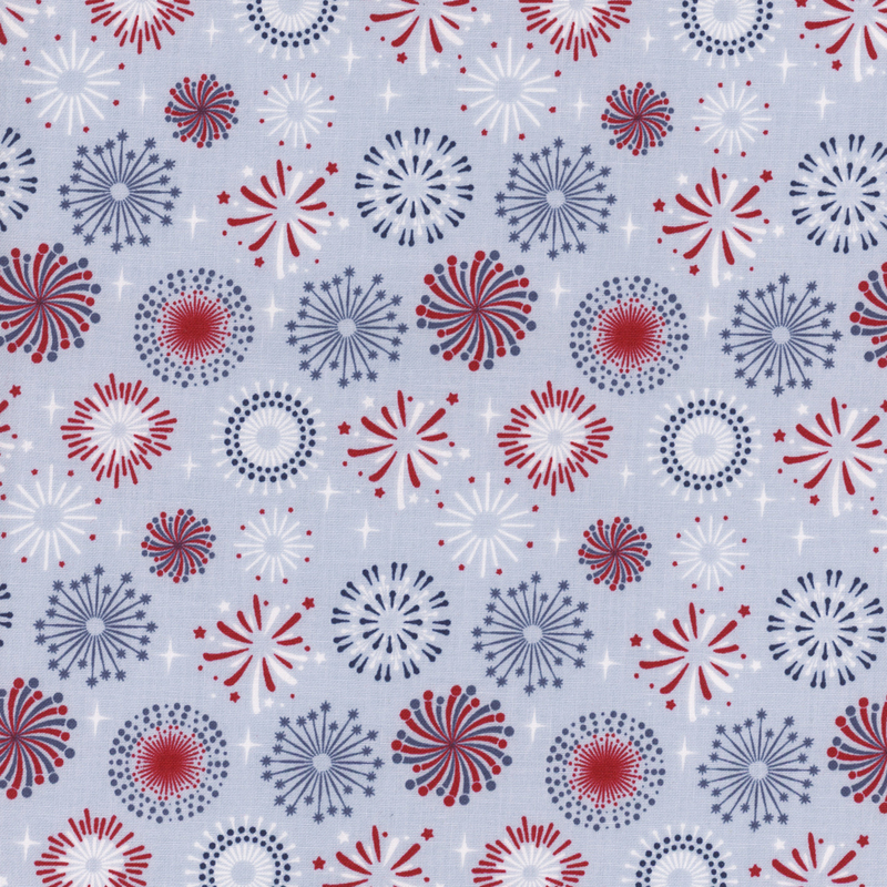 A repeating pattern of colorful fireworks in red, blue, and white against a light blue background, with various designs and shapes of fireworks scattered evenly throughout.