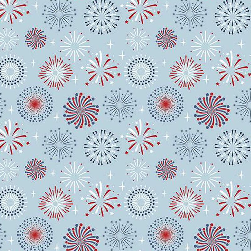 A repeating pattern of colorful fireworks in red, blue, and white against a light blue background, with various designs and shapes of fireworks scattered evenly throughout.