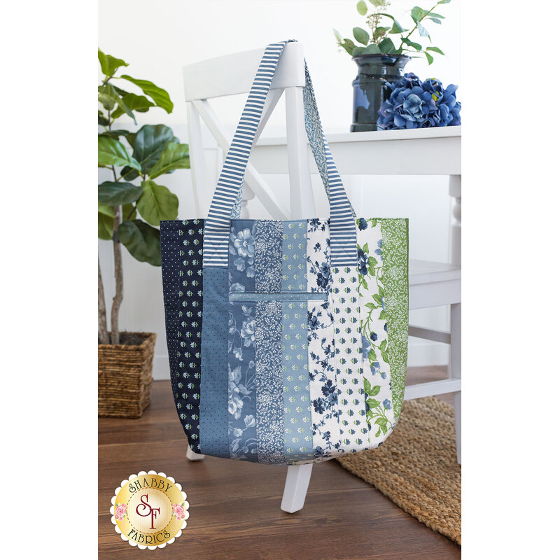 The completed jelly roll tote, hung from a white chair and staged with coordinating decor and foliage.