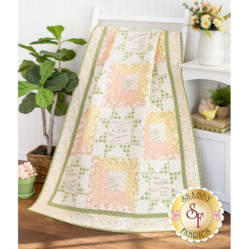 A shot of the completed Patchwork Sentiments quilt in Flower Girl, artfully draped over a white quilt ladder among coordinating furniture and decor to demonstrate flow and form.