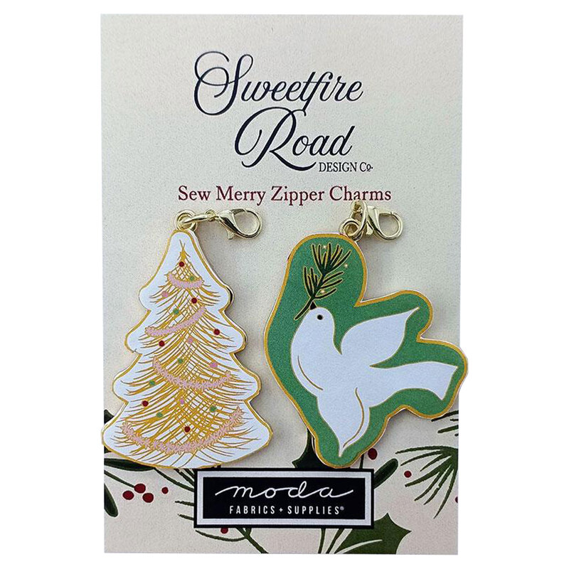 A packaging card featuring two zipper charms: one shaped like a decorated Christmas tree and the other shaped like a white dove. The card is labeled Sweetfire Road Design Co and Sew Merry Zipper Charms, with a logo for Moda Fabrics & Supplies displayed at the bottom.