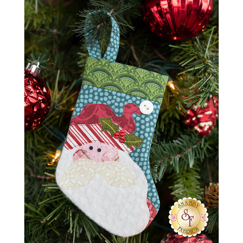 The completed Santa stocking, hung on a green Christmas tree decorated with red and green bulbs.