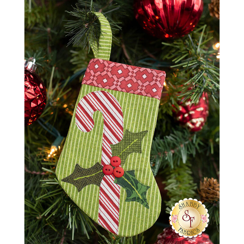 The completed candy cane stocking, hung on a green Christmas tree decorated with red bulbs.