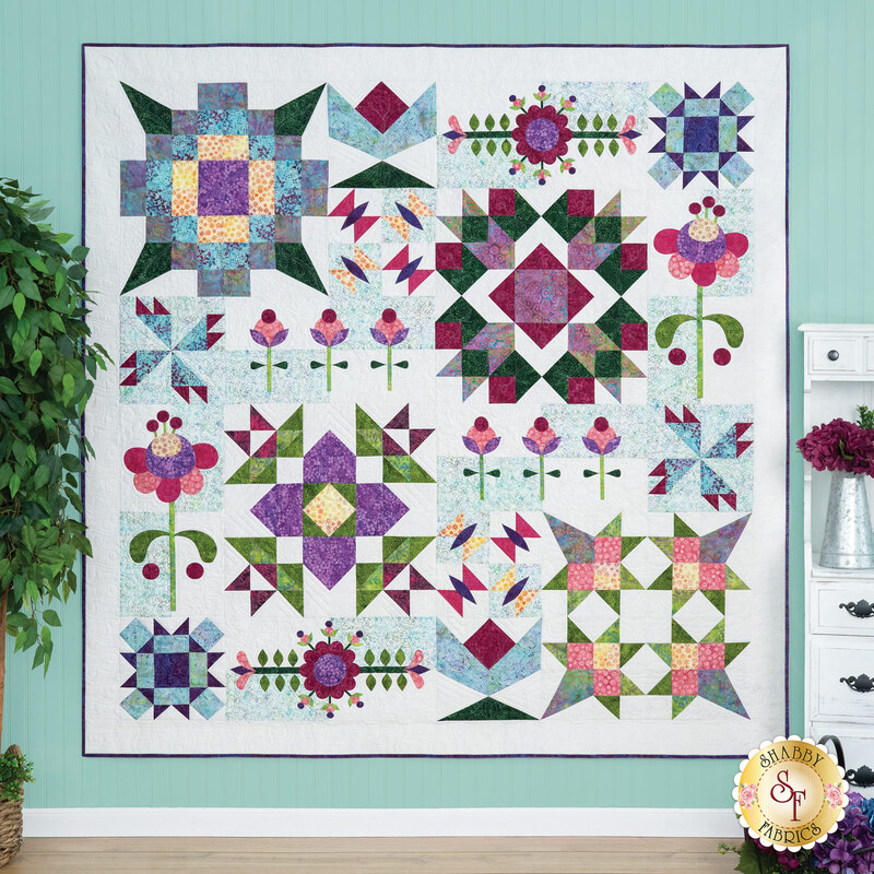 The completed Abide quilt colored in Floral Fun batik fabrics, hung on a blue paneled wall and bordered by coordinating floral decor.