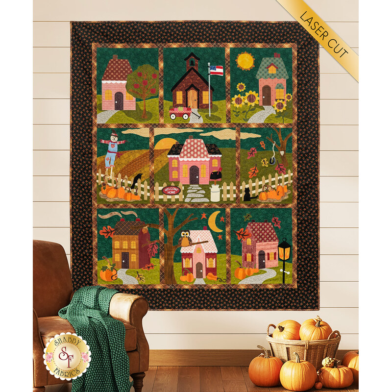 The completed Welcome Home in Autumn quilt colored in deep autumnal colors, hung on a paneled wall and staged with coordinating fall décor.