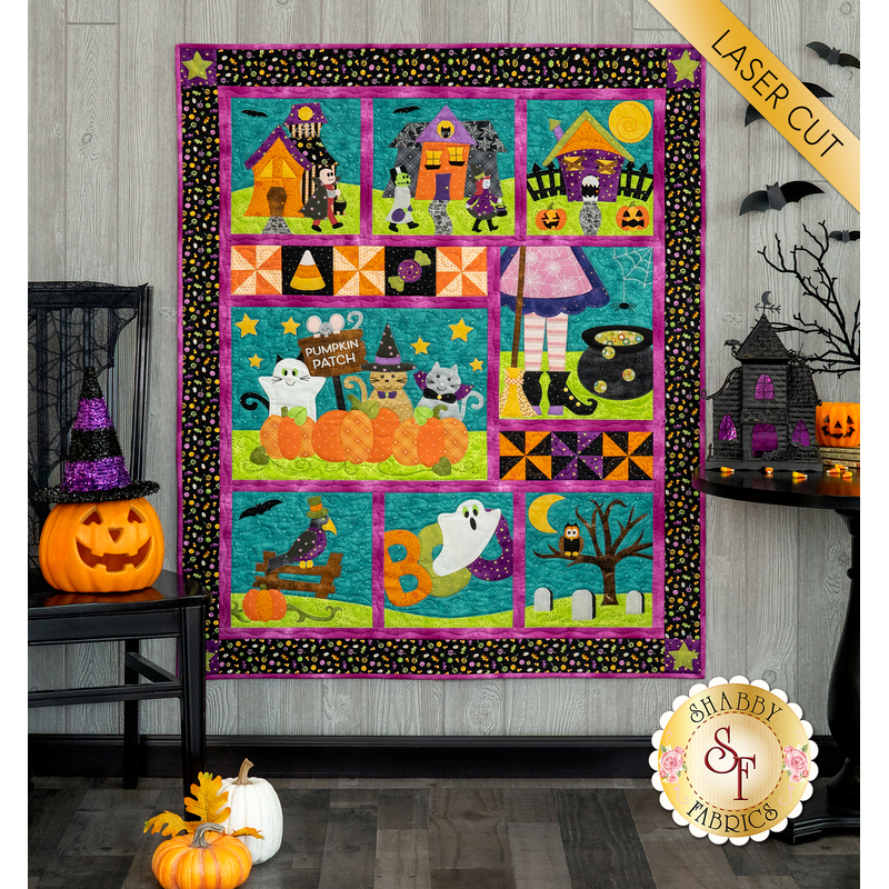 The completed Spooktacular Night Out quilt in cheerful Halloween colors, hung on a paneled wall beside coordinating festive decor like jack-o-lanterns and bats. A yellow banner in the upper right hand corner reads 