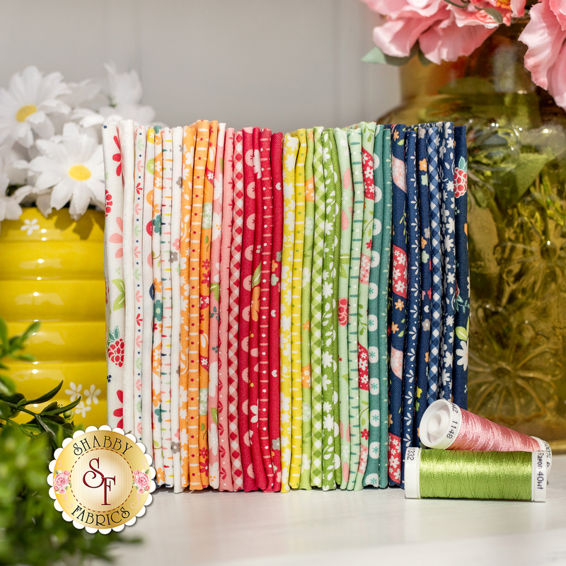 Colorful fabric bundle arranged neatly, accompanied by spools of green and pink thread and decorative flowers.