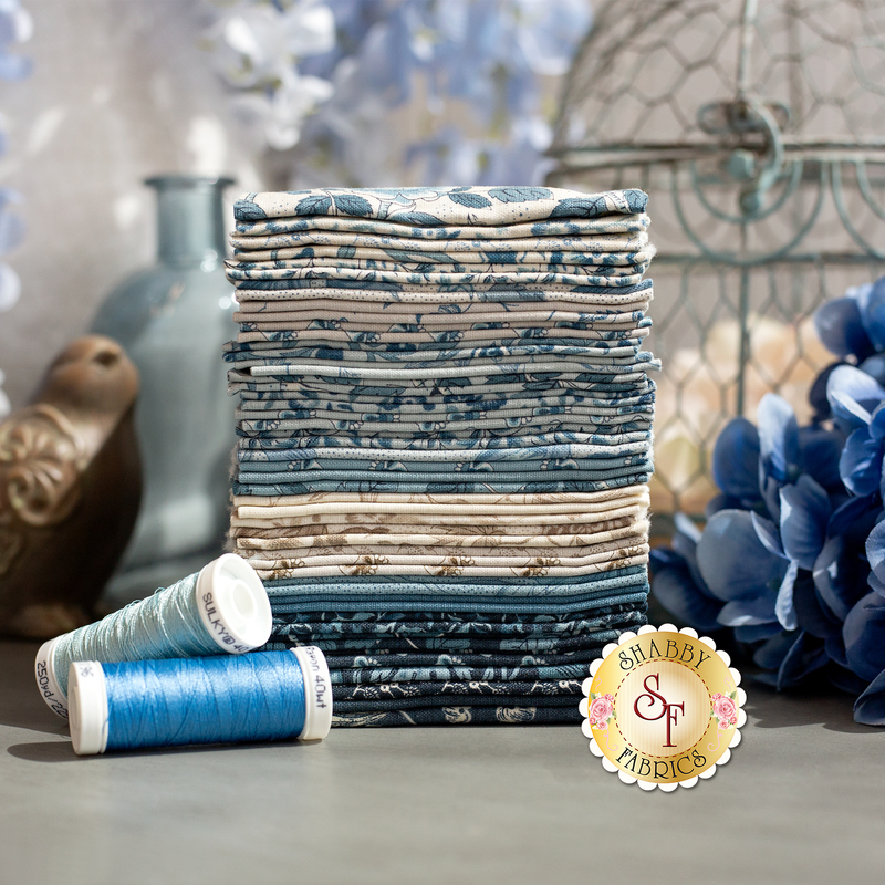 Stack of patterned fabric squares in blue and cream, with matching spools of thread nearby.