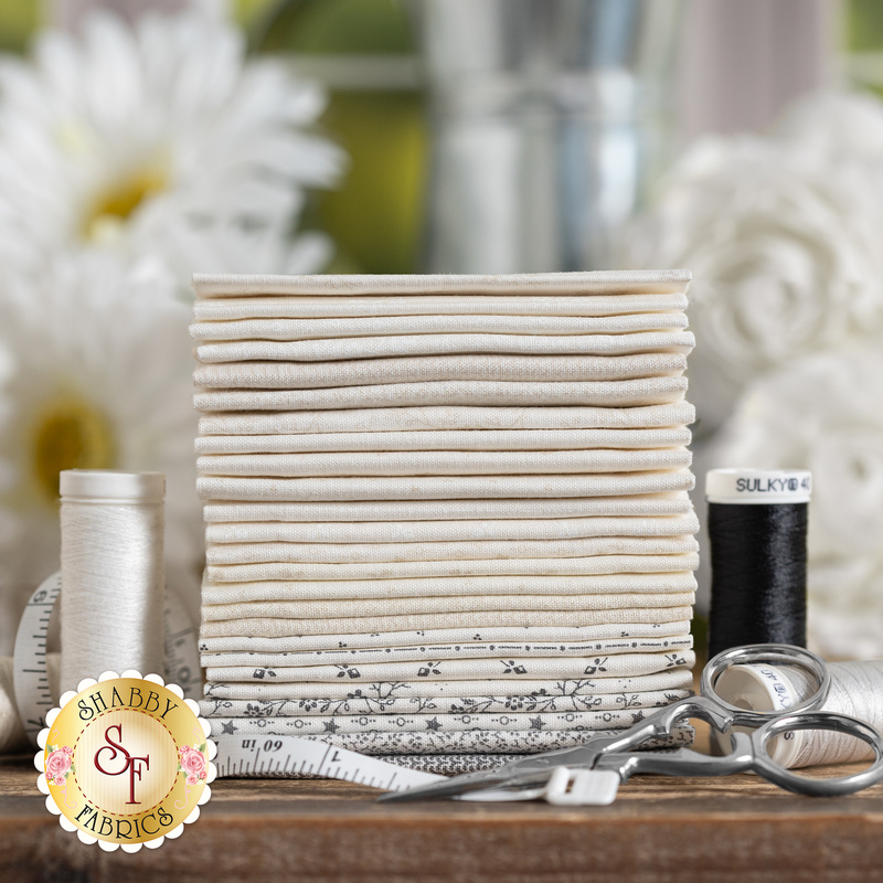 styled photography of a stack of neatly arranged fabric squares in white, cream and floral patterns with sewing supplies, including scissors and spools of thread.