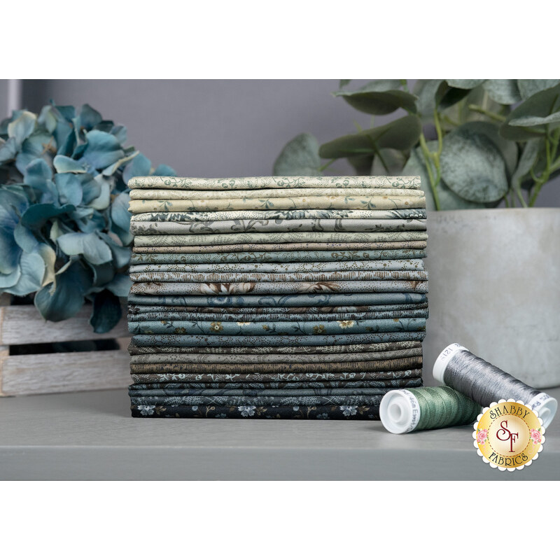 A stack of the fabric included in the Dark & Stormy FQ set, with a plant, flowers, and thread.