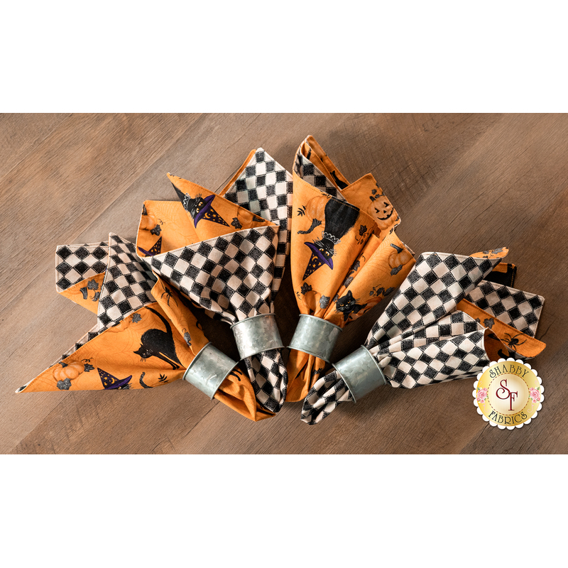 A top down shot of the four napkins slightly fanned out on a wood table top. A Shabby Fabrics logo can be seen in the lower right corner.