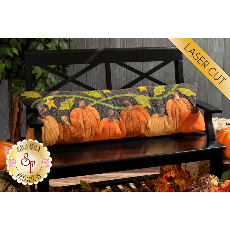 The completed Pumpkin Patch Pillow in flannel and cotton fabric, staged on a black bench surrounded by autumn leaves and decorations.