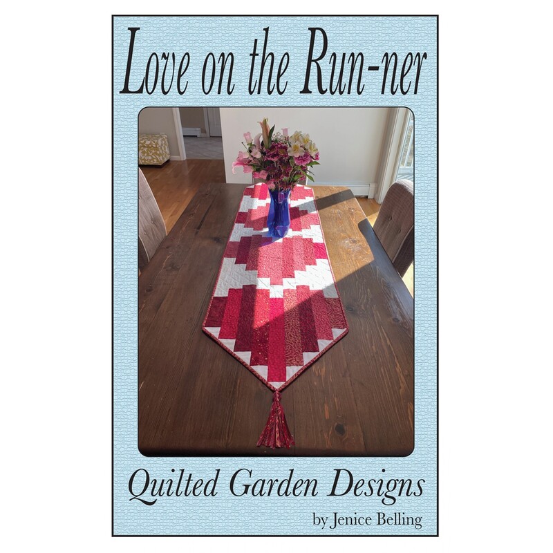 Front cover of the pattern showing the completed project in red, pink, and white, staged on a dark wood table.