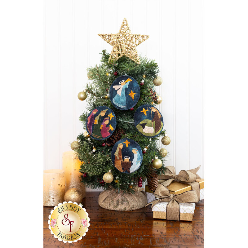 The four completed wool ornaments hung on a small tree, displayed on a wood table with coordinating decor.