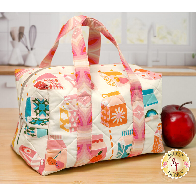 The completed Insulated Lunchbox colored in vibrant fabrics from the Juicy collection by Moda Fabrics. The project is staged on a kitchen counter with a red apple.