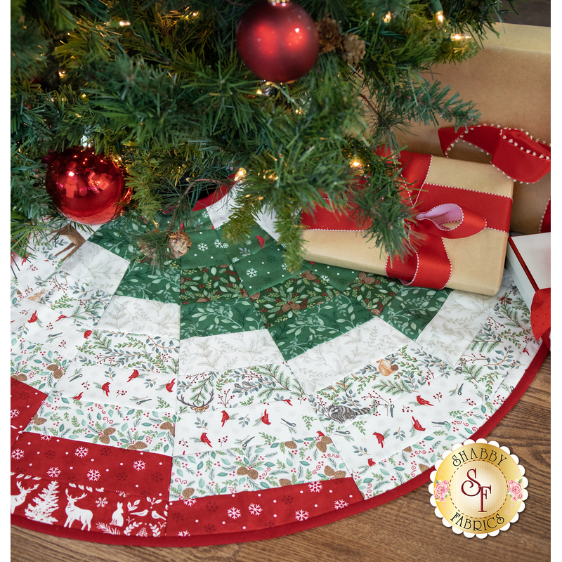 A festive quilted tree skirt with red and green patterns, placed under a decorated Christmas tree.