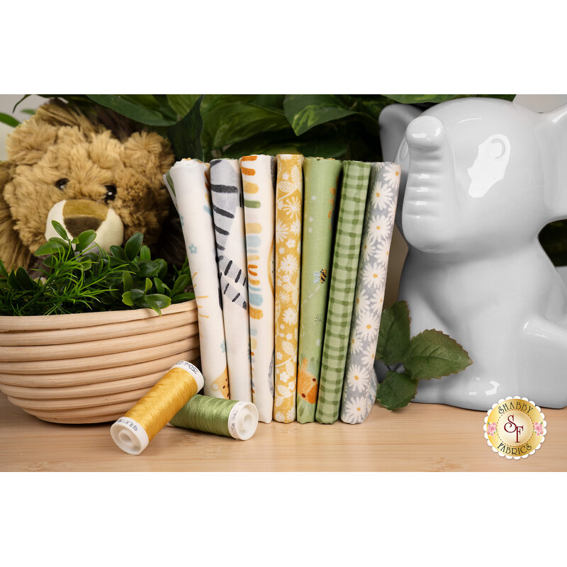 A stack of Safari themed fabrics that are included in the Sunny Safari collection, with an elephant and a lion and greenery and thread.
