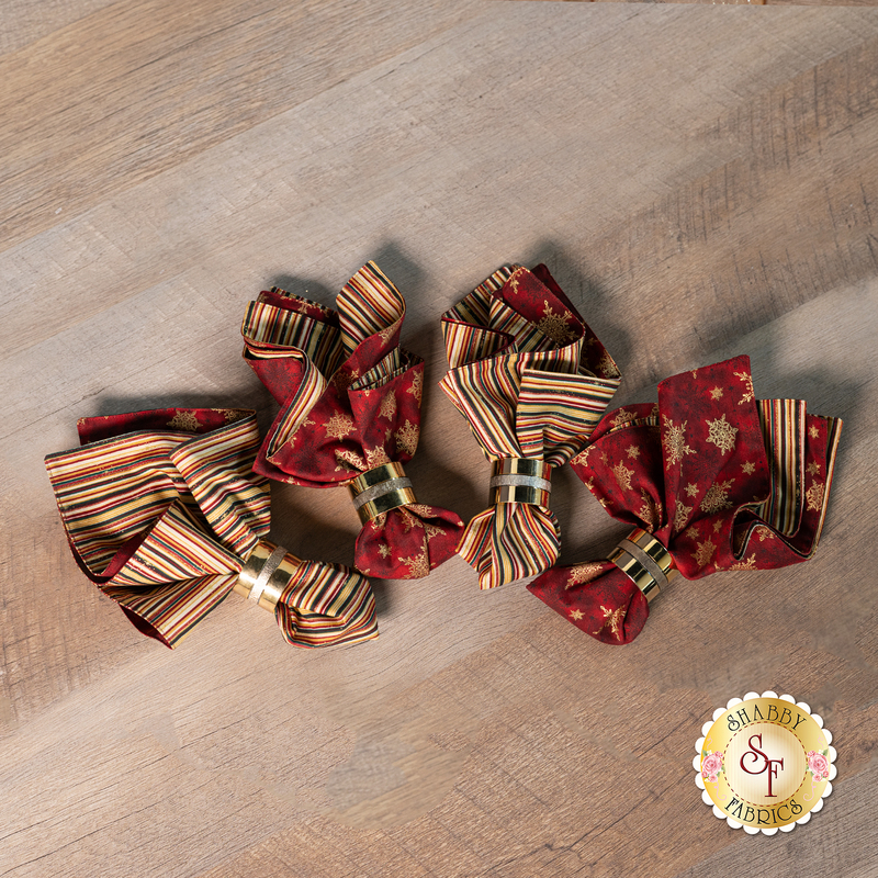 A top down shot of the four napkins slightly fanned out on a wood table top. A Shabby Fabrics logo can be seen in the lower right corner.