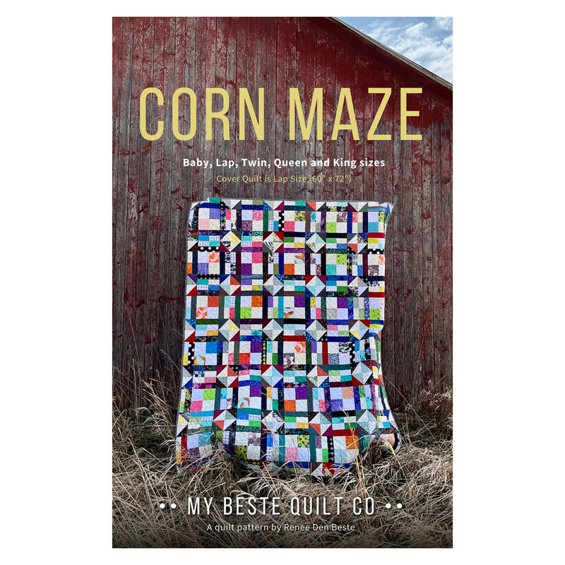 The front of the Corn Maze pattern featuring the finished quilt held up in front of a weathered barn.