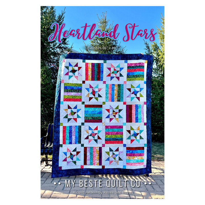 The front of the Heartland Stars pattern featuring the finished quilt being held up in front of pine trees in a backyard.