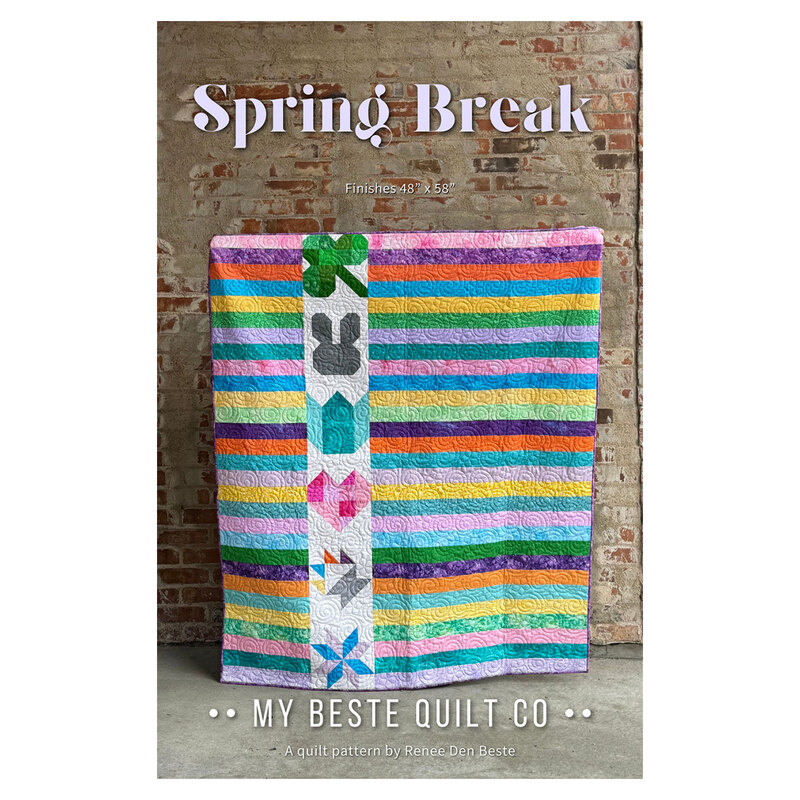 The front of the Spring Break pattern featuring the finished quilt being held up in front of a worn brick wall.