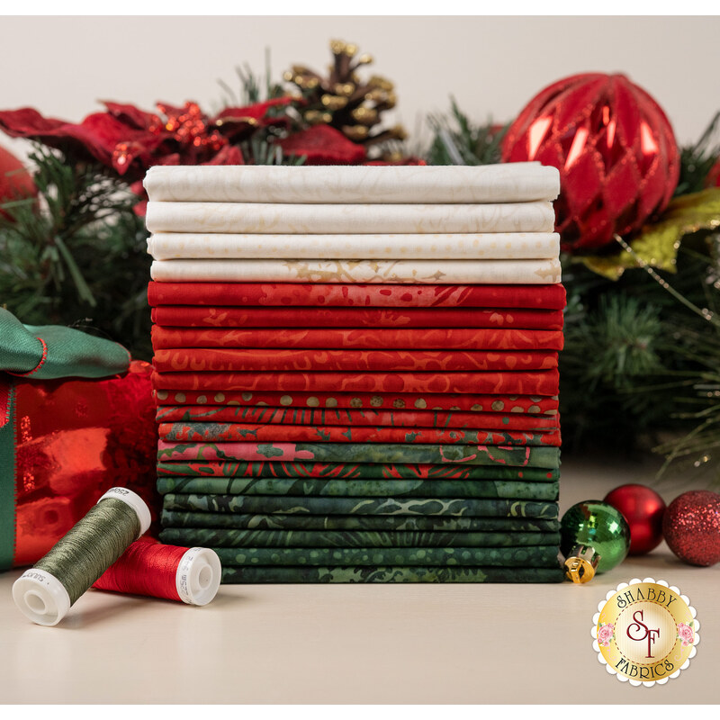 A stack of the fabrics included in the Tonga Mistletoe FQ set, with a holiday garland and ornaments and presents and thread.