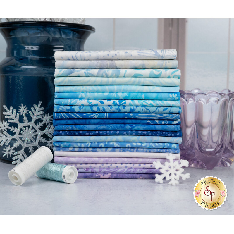 A stack of the fabrics included in the Tonga Crystal collection, with vases and snowflakes and thread.