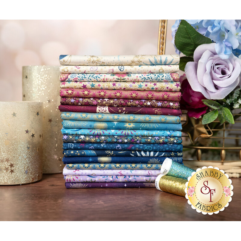 A stack of fabrics in the Luna Collection, with candles and thread and flowers in a basket.