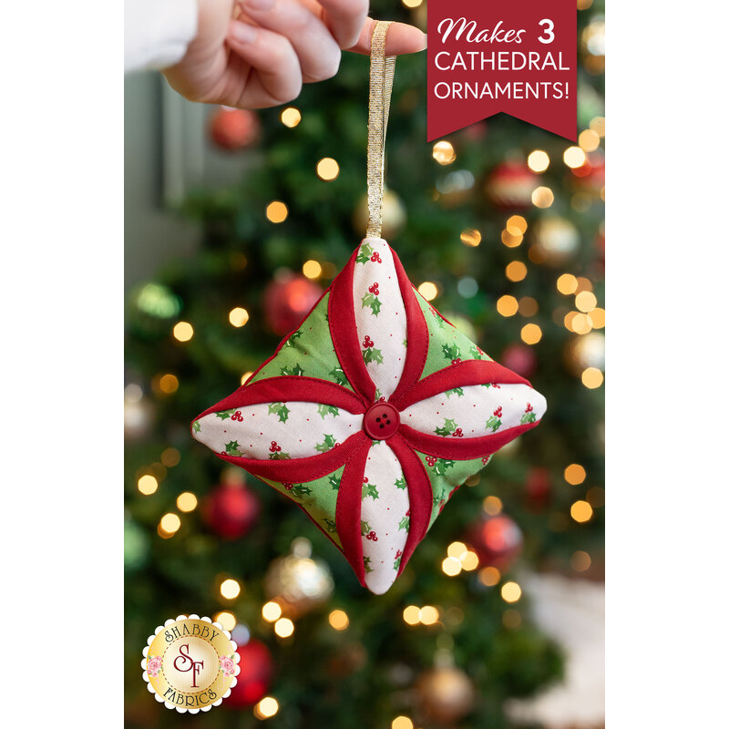 A close up on one of the completed ornaments, colored in white, red, and light green fabrics and staged in front of a lit Christmas tree.