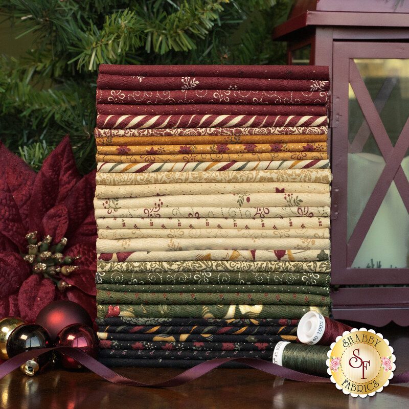 A Vintage Christmas FQ in a stack with a lantern, a flower, baubles, thread, and ribbon.