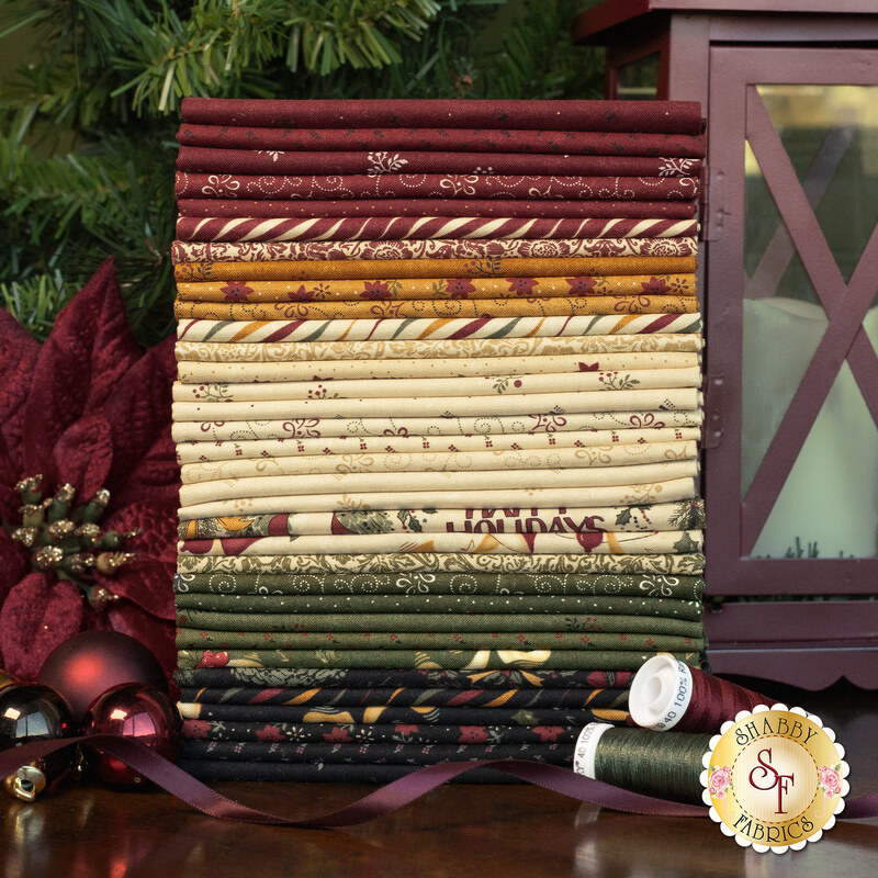 A Vintage Christmas FQ in a stack with a lantern, a flower, baubles, thread, and ribbon.