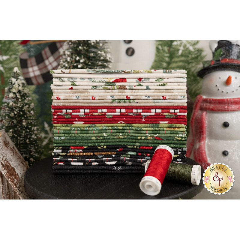 A stack of winter-themed fabrics, with a snowman and trees and thread.
