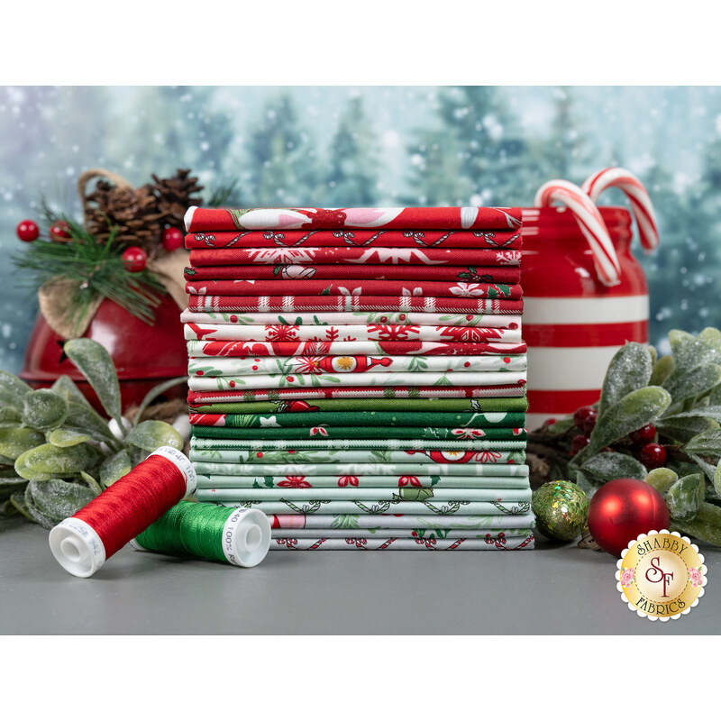 A stack of holiday themed fabric, with mistletoe and holly and candycanes and a jar and thread and ornaments.