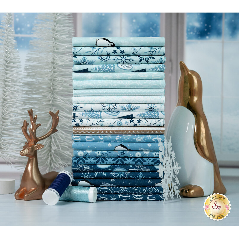 A stack of winter-themed fabrics with a window and snow and trees and snowflakes and a penguin and a reindeer and thread.