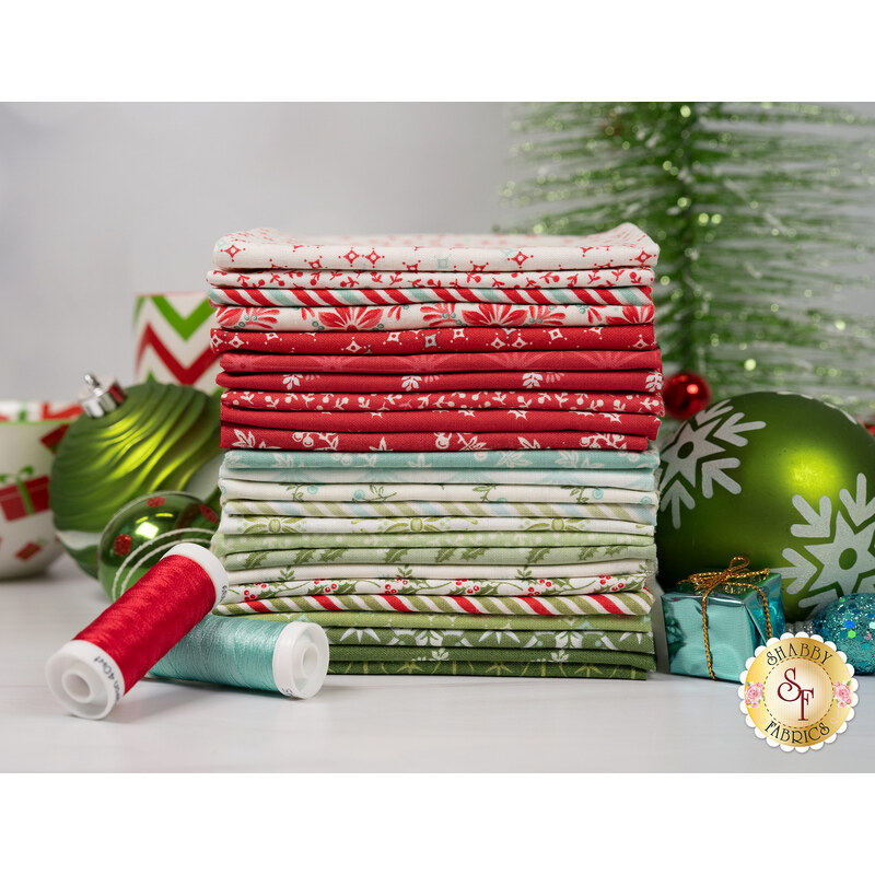 A stack of fabrics included in the Sugarberry collection, with ornaments and a tree and thread.