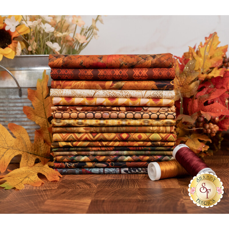 A stack of the fabrics included in the Falling Leaves collection, with leaves and a jug and flowers and thread.