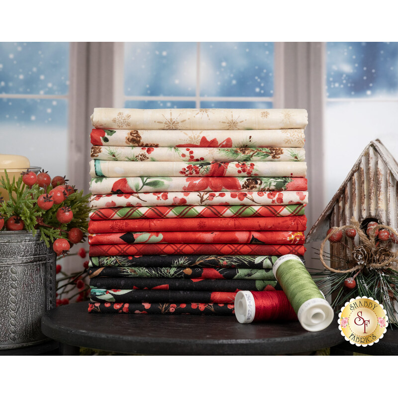 A stack of the fabrics included in the Cardinal Celebration collection, with berries and a candle and a birdhouse and thread.