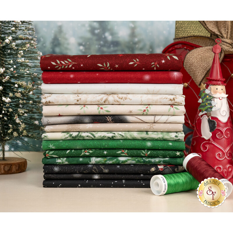 A stack of Christmas fabrics included in the Believe collection, with a sled and trees and Santa and thread.