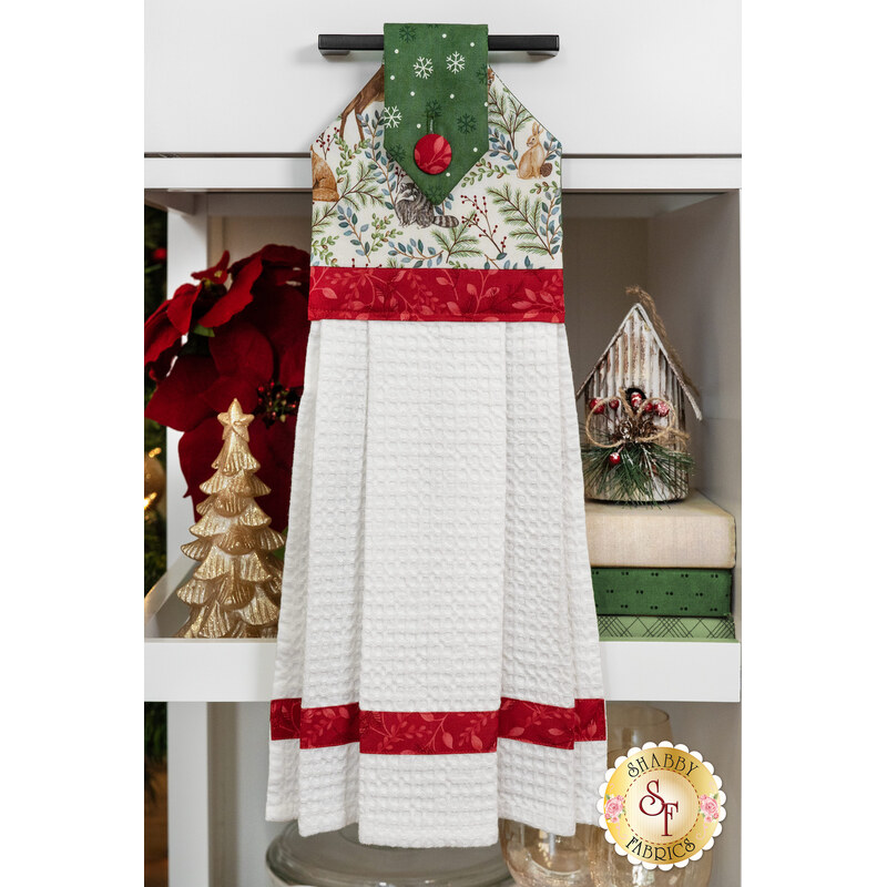 A festive kitchen towel with a green decorative top, red accents, and patterned white fabric.