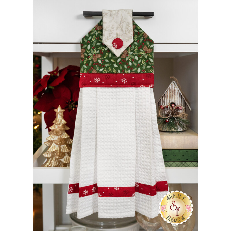 A festive kitchen towel with a green and red patterned top and textured white bottom hanging decoratively.