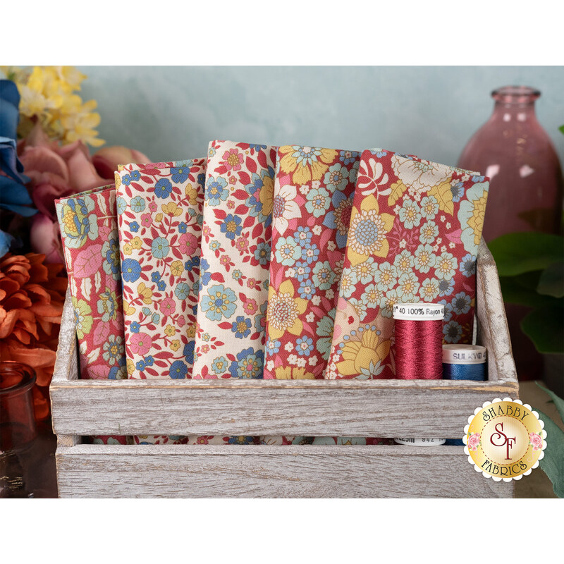 A stack of the Burgundy and Pink Wallflower 5 FQ set with a bottle and thread and a wooden box and flowers
