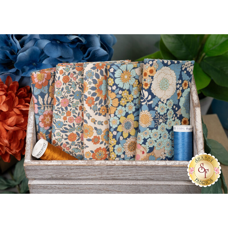 A stack of the Blue Wallflower 5 FQ set with thread and a wooden box and flowers.