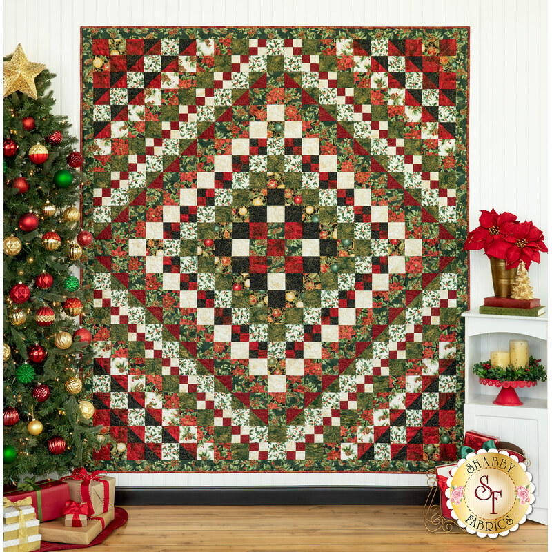 A diamond-patterned quilt in red, green, and white is displayed near a Christmas tree and decorations.